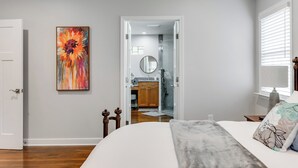 Un dormitorio con cama, un cuadro, una puerta y un baño a la vista a través de una puerta abierta.