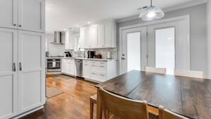 Una cocina moderna con armarios blancos, una mesa de comedor de madera y una lámpara colgante.