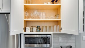 Una cocina con microondas, estantes de madera con cristalería y una cafetera.