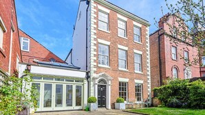 A traditional brick building with a central entrance, a conservatory, and a paved courtyard.