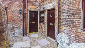 Une ruelle étroite aux murs de briques, une porte en bois portant l’inscription « Krikete Studio », et un banc en métal blanc.