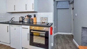 Une cuisine compacte avec des meubles blancs, un four encastré et un plan de travail équipé de divers ustensiles.