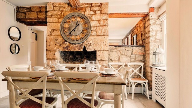 A rustic dining area with a stone wall, a round clock, and white furniture.