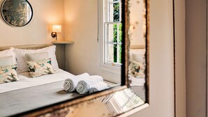 A neatly made bed with white linens and decorative pillows, a bedside lamp, and a window with a view of greenery.