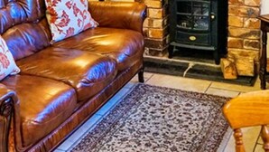 Un salon avec un canapé en cuir, un tapis à motifs, une cheminée et une horloge murale.