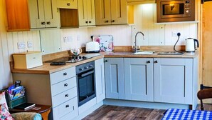 Een compacte keuken met een magnetron, oven, gootsteen en een houten aanrecht.