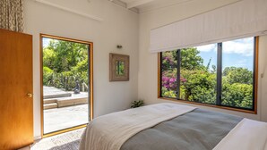A bedroom with a large window, a bed, a door, and a small plant.