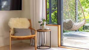 A cozy room with a wooden chair, a small round table, a hanging chair, and a large window with a view of greenery.