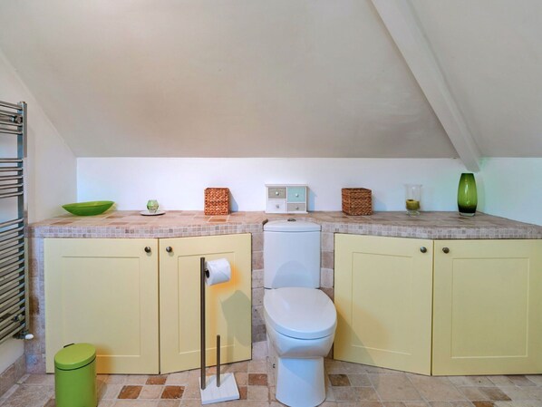 A compact kitchen with a toilet, a trash bin, and a small countertop with a radio and decorative items.