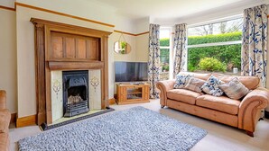 A living room with a fireplace, a television, a sofa, and a large window with curtains. - Wonderful  villa for 7 guests with WIFI (Colwyn Bay)