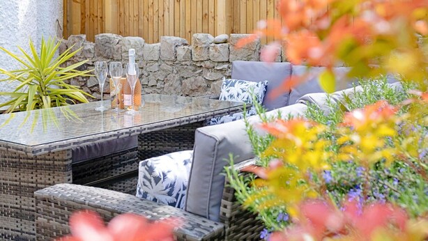 An outdoor patio with a glass-top table, wicker furniture, and a stone wall backdrop. - Wonderful  villa for 7 guests with WIFI (Colwyn Bay)