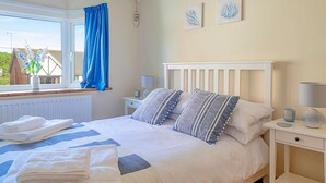 A neatly made bed with striped pillows, a bedside table with a lamp, and a window with blue curtains. - Wonderful  villa for 7 guests with WIFI (Colwyn Bay)