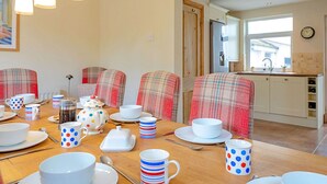 A dining area with a wooden table set for a meal, plaid-covered chairs, and a kitchen in the background. - Wonderful  villa for 7 guests with WIFI (Colwyn Bay)