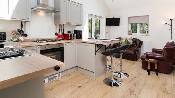 A modern kitchen with a central island, a dining area with a sofa and chairs, and a TV mounted on the wall.