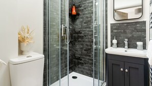 A modern bathroom with a glass-enclosed shower, a white toilet, a dark wooden cabinet, and a mirror above the sink.
