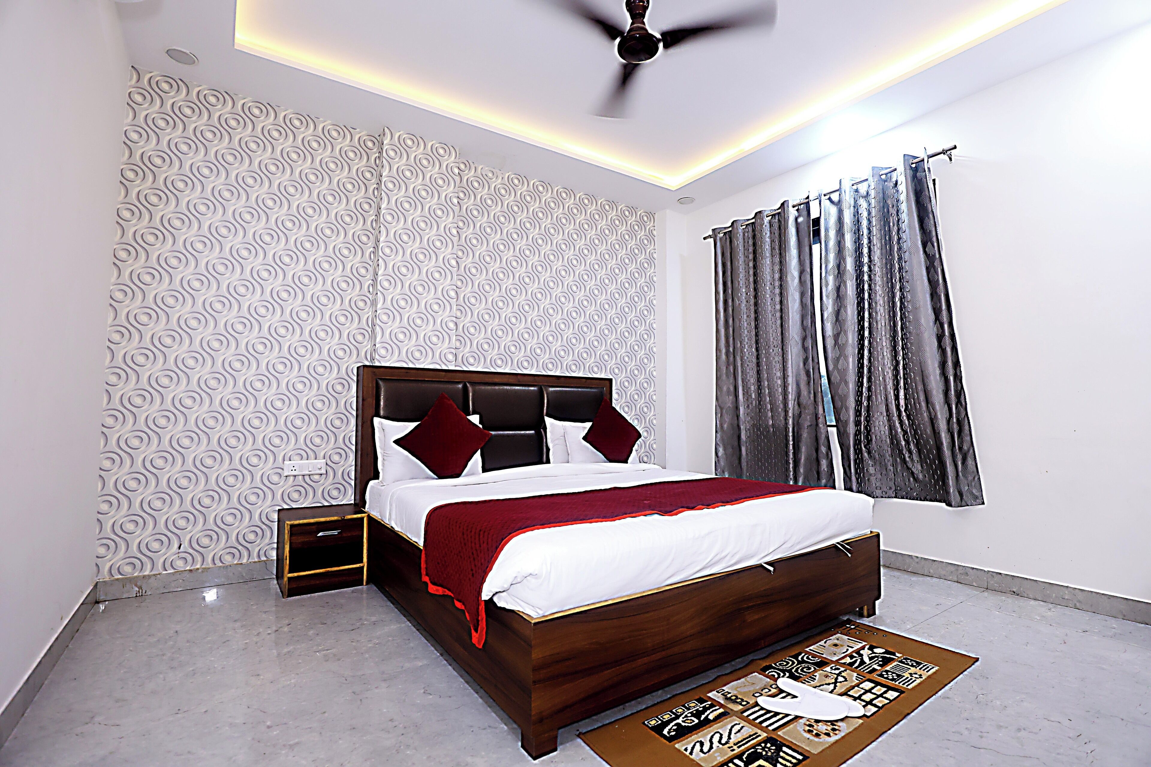 A modern bedroom with a wooden bed, patterned wallpaper, a ceiling fan, and a window with curtains.