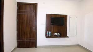 A room with a wooden door, a mounted TV, and a shelf with bottles and glasses. - Hotel Akash Inn  Hotel Near Taj Mahal (Agra)