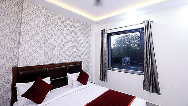A hotel room with a bed, a window with curtains, a ceiling fan, and patterned wallpaper. - Hotel Akash Inn  Hotel Near Taj Mahal (Agra)