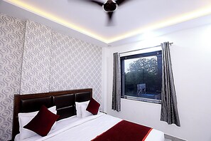 A hotel room with a bed, a window with curtains, a ceiling fan, and patterned wallpaper. - Hotel Akash Inn  Hotel Near Taj Mahal (Agra)