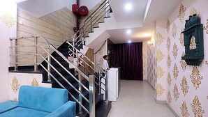 A staircase with a handrail, a blue sofa, and a person standing near a white counter. - Hotel Akash Inn  Hotel Near Taj Mahal (Agra)