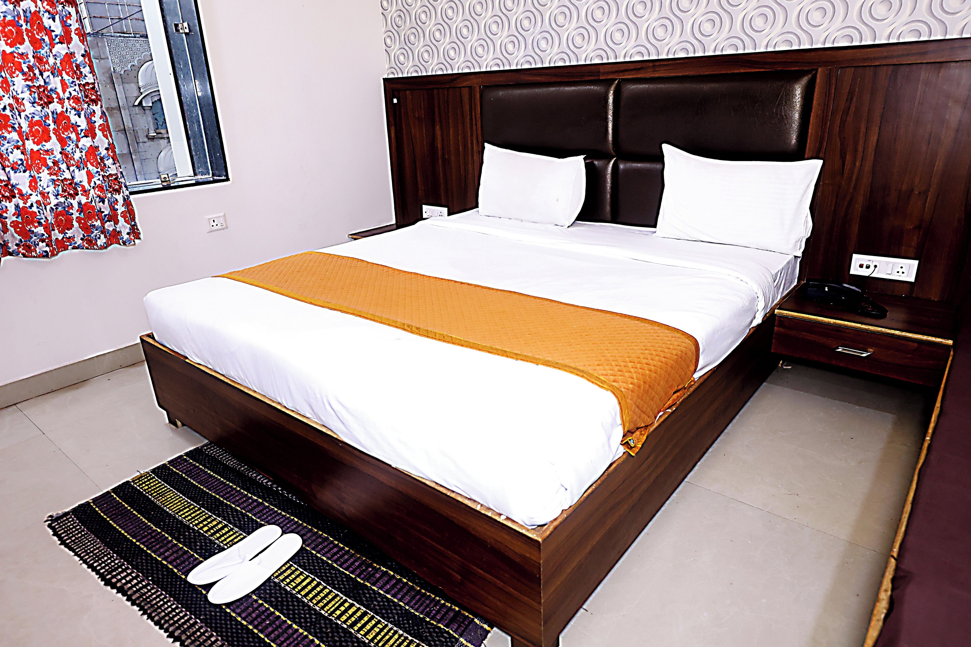 A neatly made bed with a white and orange bedspread, a wooden headboard, and a bedside table with a phone.