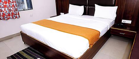 A neatly made bed with a white and orange bedspread, a wooden headboard, and a bedside table with a phone.