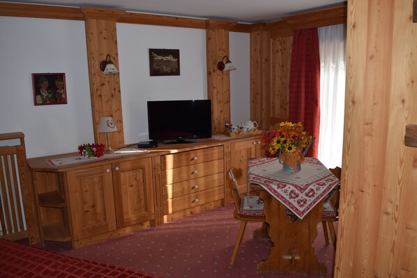 A wooden cabin interior with a dining table, chairs, a TV, and a window with curtains. - Hotel Cime Bianche (Valtournenche)