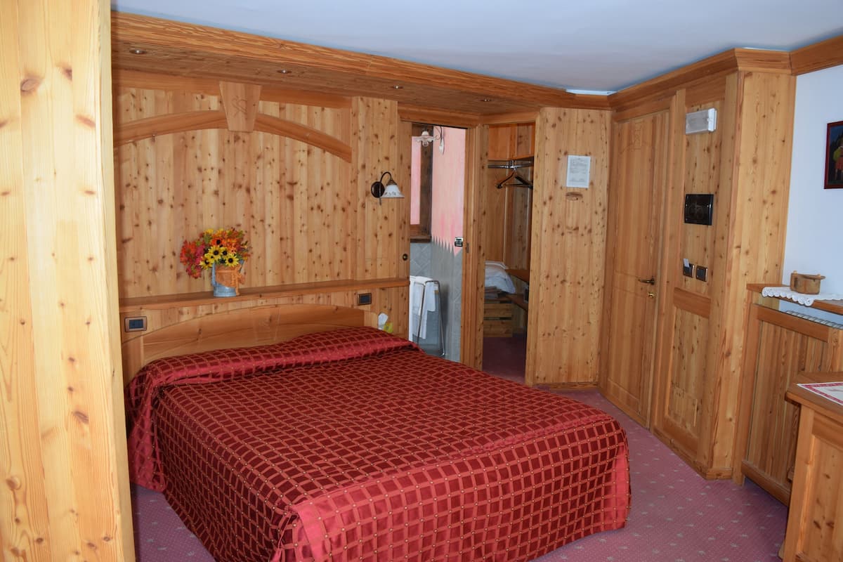 Ein Zimmer aus Holz mit einem Bett, einem Holzschrank und einem kleinen Tisch mit Blumen.