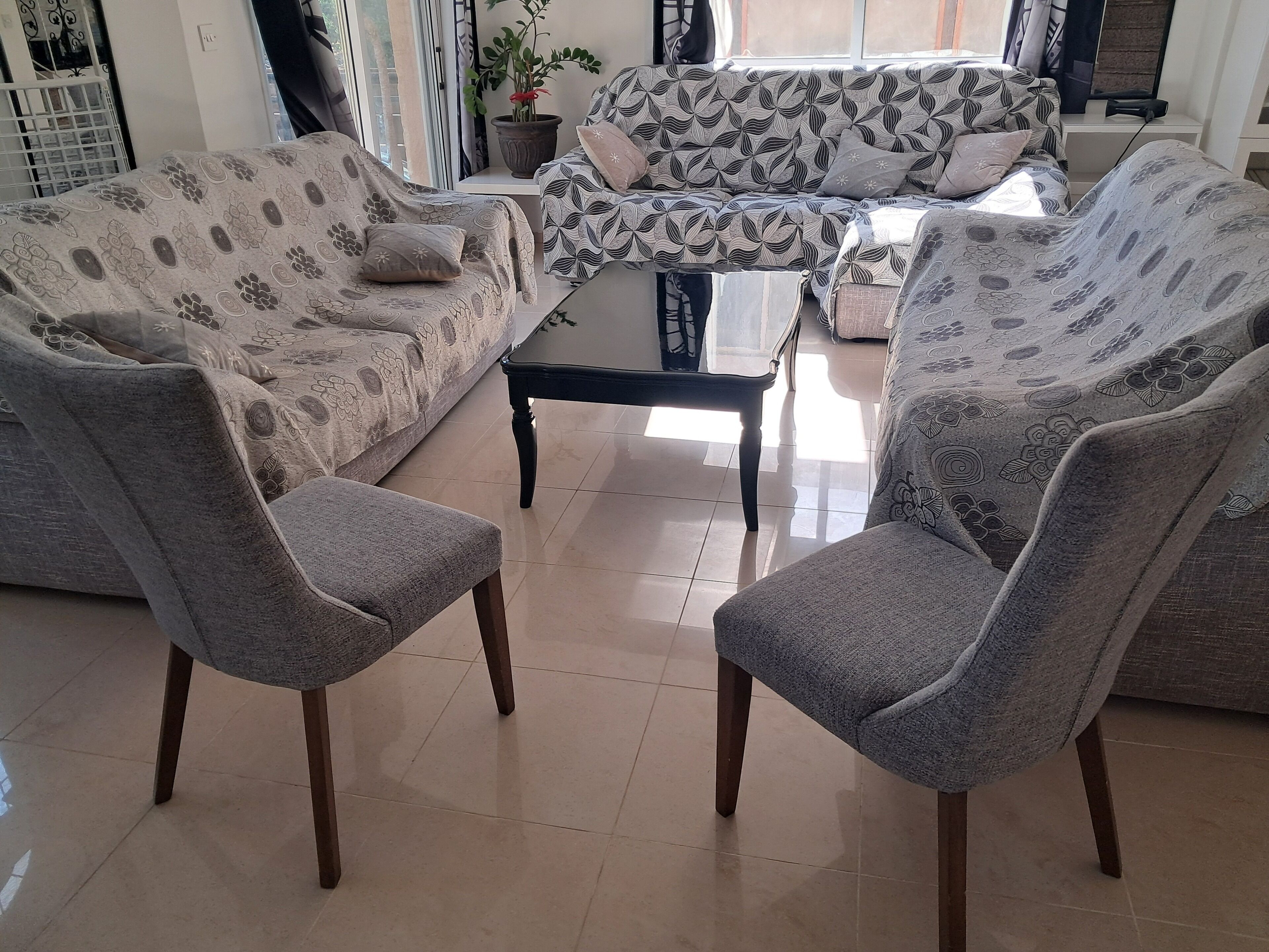 A living room with two grey armchairs, a patterned sofa, and a glass coffee table.