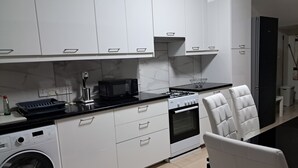 Una cocina moderna con armarios blancos, una encimera negra, un microondas, una estufa y una lavadora.