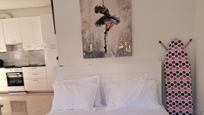 Habitación de hotel con cama, almohadas blancas, una toalla doblada, un cuadro de una bailarina y una plancha con estampado de lunares.
