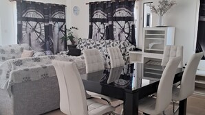 Una sala de estar moderna con comedor, que incluye un sofá, una mesa de comedor con sillas, un televisor y una planta decorativa.