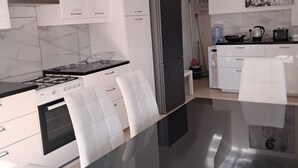 Una cocina moderna con armarios blancos, encimera negra y una mesa de comedor de cristal.
