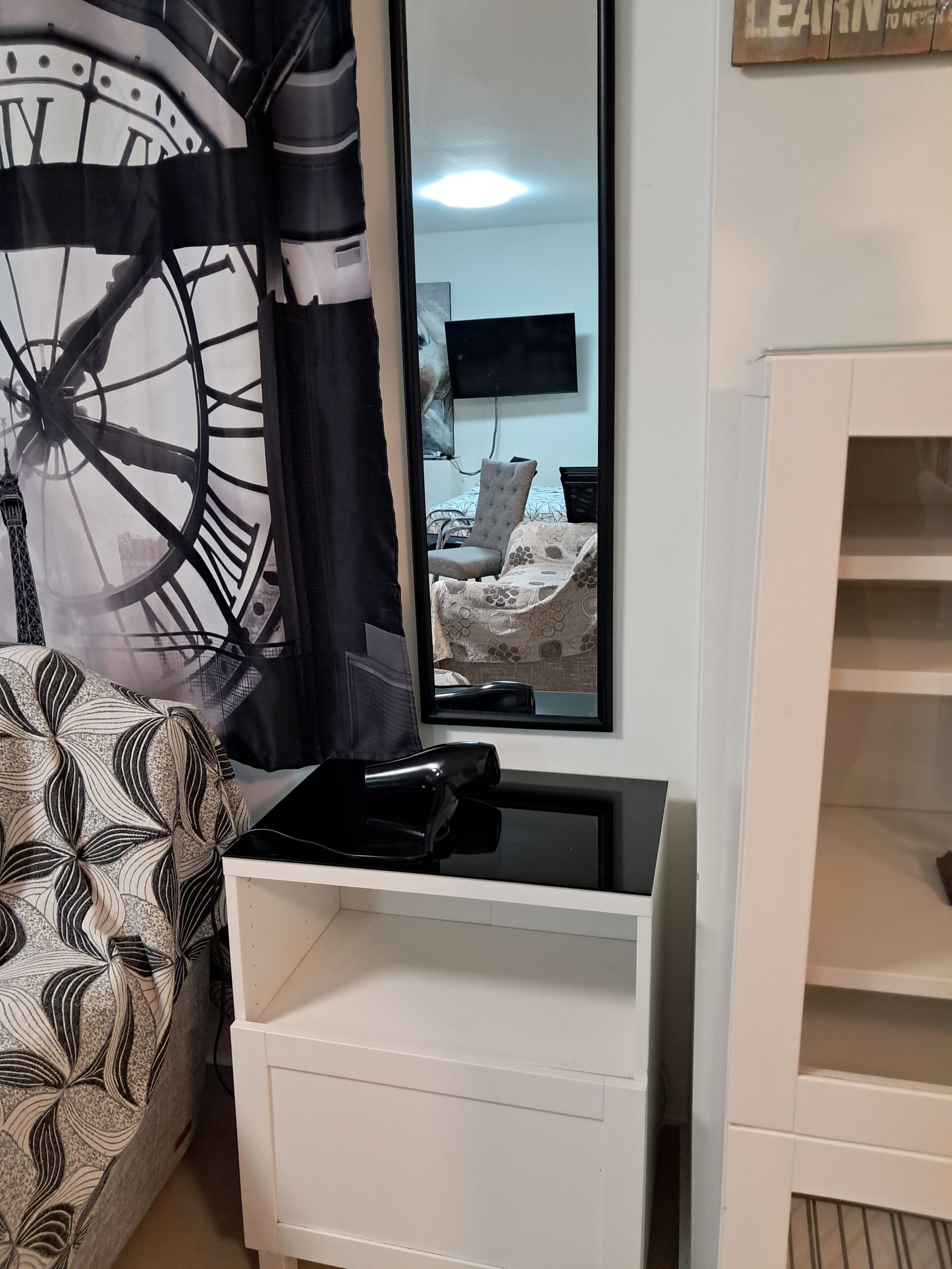 A room with a bed, a white dresser, a mirror, and a wall-mounted TV.