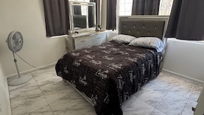 Un dormitorio con cama, cómoda, espejo, ventilador y ventana con cortinas.