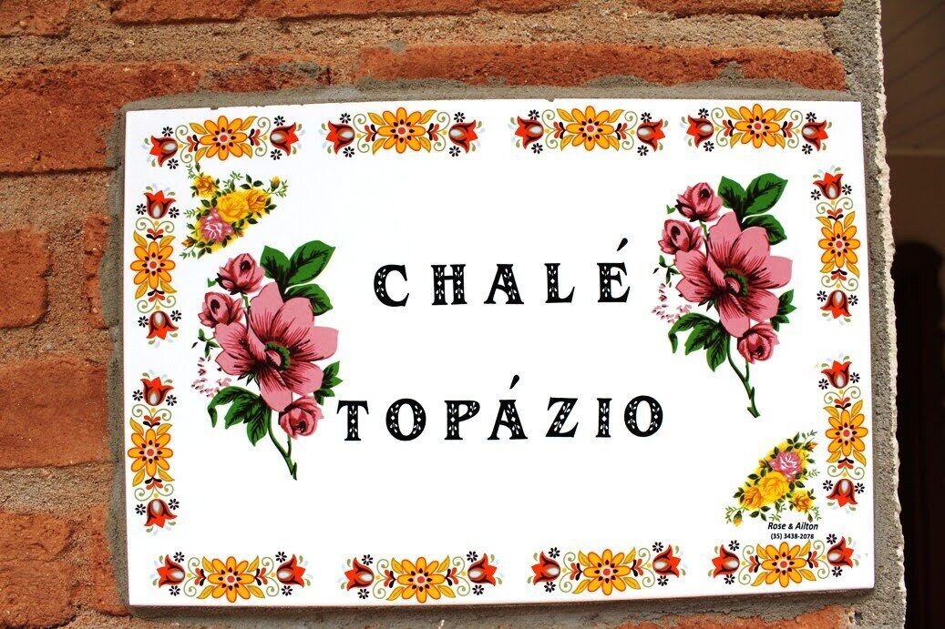 Un letrero decorativo con motivos florales y el texto 'Chalet Topázio'.