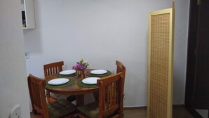 A dining area with a round table set for four, wooden chairs with green cushions, a vase with purple flowers, and a wooden partition on the right. - Chalé Topázio (Monte Verde)