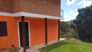 A two-story building with an orange facade, a visible door, and a balcony. - Chalé Topázio (Monte Verde)
