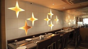 Un restaurante con una barra alargada, luces de pared en forma de estrella y un candelabro moderno.