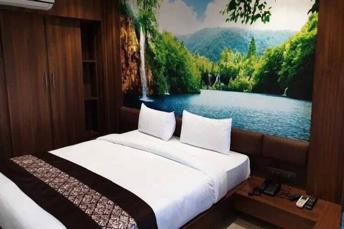 A bedroom with a large bed, a wooden wardrobe, and a mural of a forest and lake.