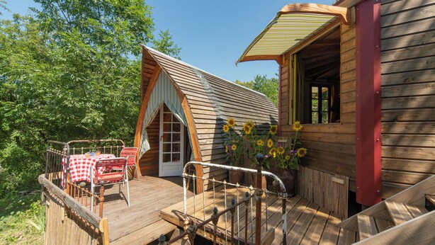 Een houten vakantiehuisje met een terras, een rode deur en een tafel met een rood-wit geruit tafelkleed.