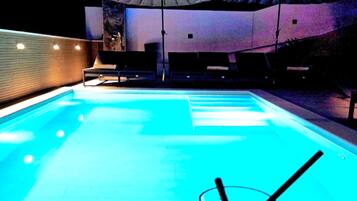 A swimming pool with a glass of water and straws, surrounded by lounge chairs and umbrellas.
