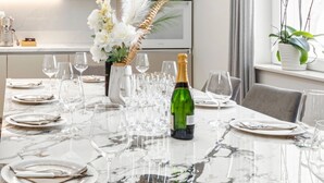 A marble dining table set with wine glasses, plates, and cutlery, a green champagne bottle, and a vase with white flowers.