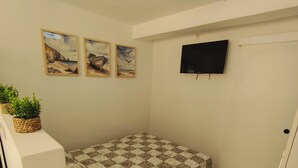 Une petite chambre à coucher, bien rangée, avec un lit, un téléviseur et trois tableaux encadrés accrochés au mur.