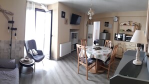 Una sala de estar con sofá, una mesa de comedor con sillas, una zona de cocina con electrodomésticos y un espejo en la pared.