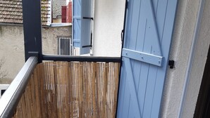 Un balcón con una puerta azul, una valla de bambú y vistas de edificios cercanos.