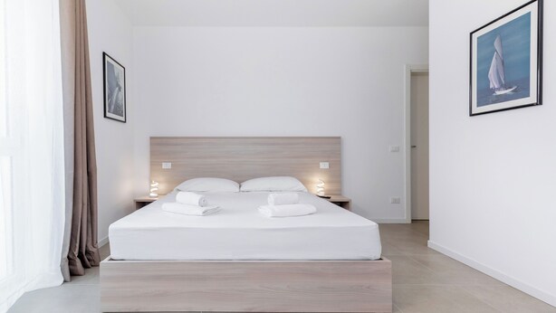 A modern bedroom with a wooden headboard, a neatly made bed with white linens, and two bedside lamps. - Appia (Mestre)