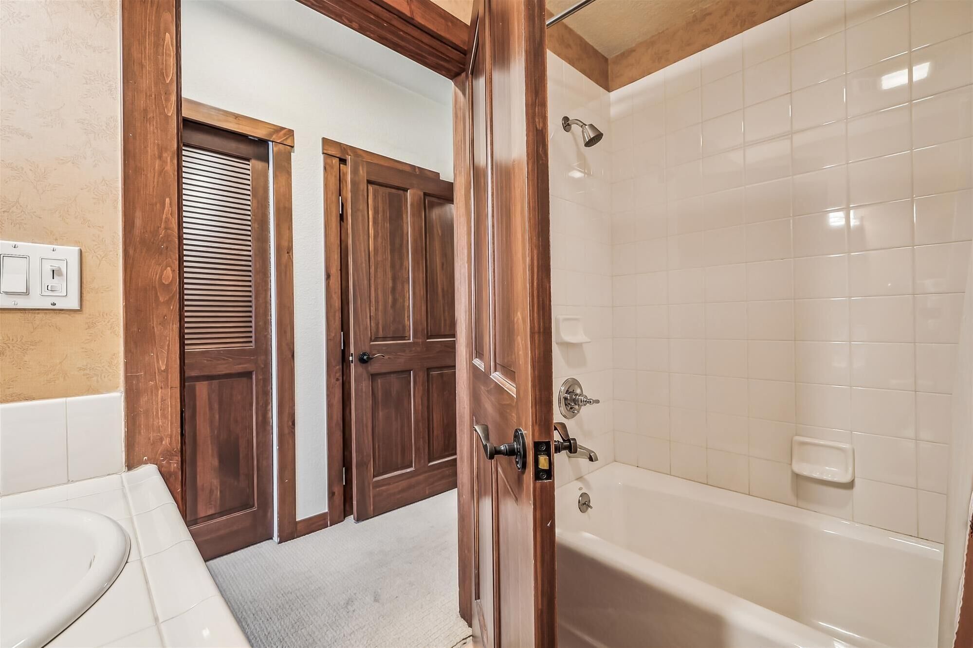 Un baño con bañera, puertas de madera y zona de ducha con azulejos blancos.