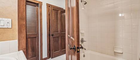 Un baño con bañera, puertas de madera y zona de ducha con azulejos blancos.