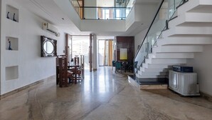 A spacious interior with a marble floor, a dining area with wooden furniture, a staircase with glass railings, and a view to the outside. - Heartland Ganga View Villa Jacuzzi &lift (Rishikesh)